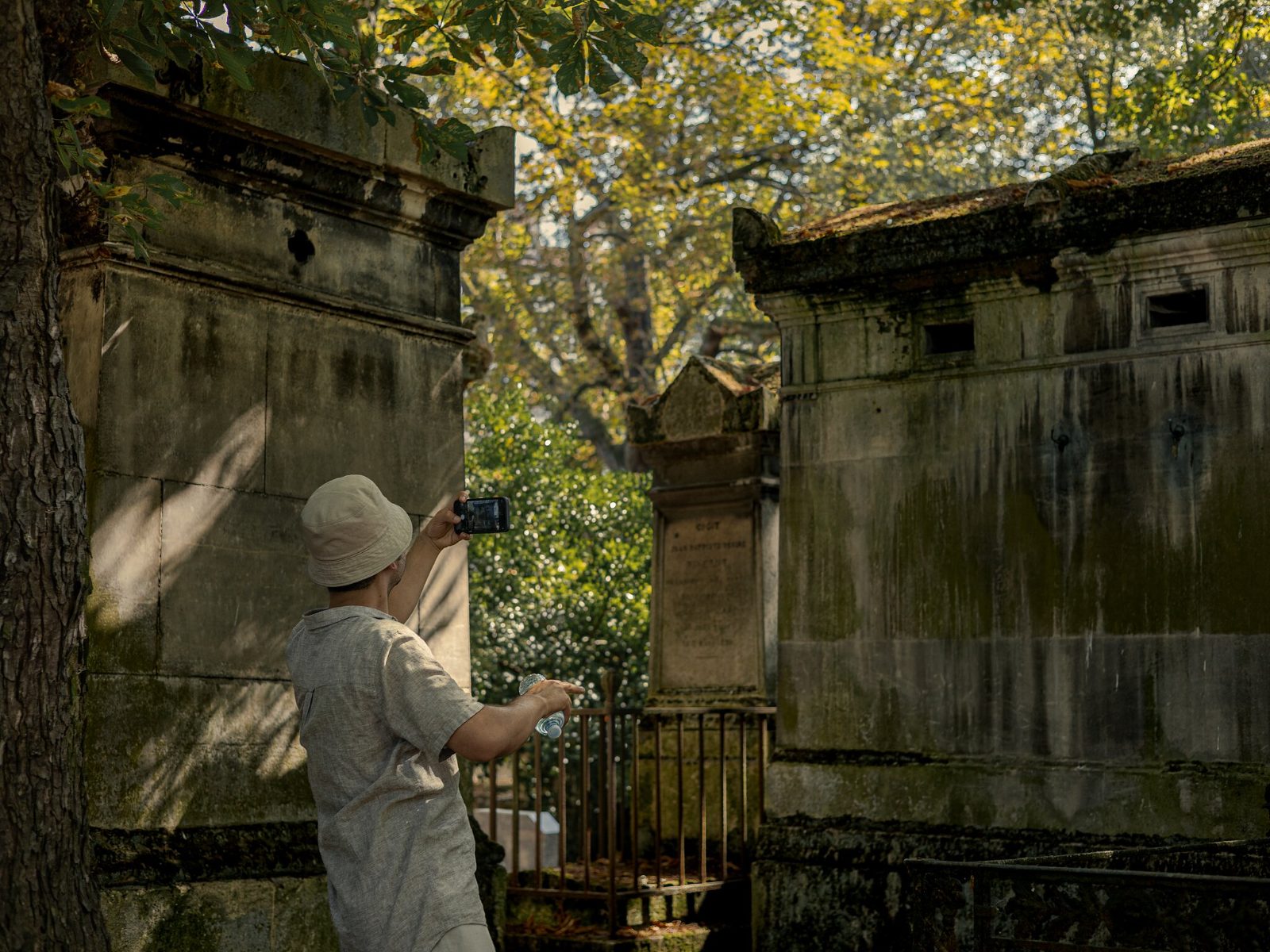 A visitor photographing a moss-covered family vault on a narrow path between tombs