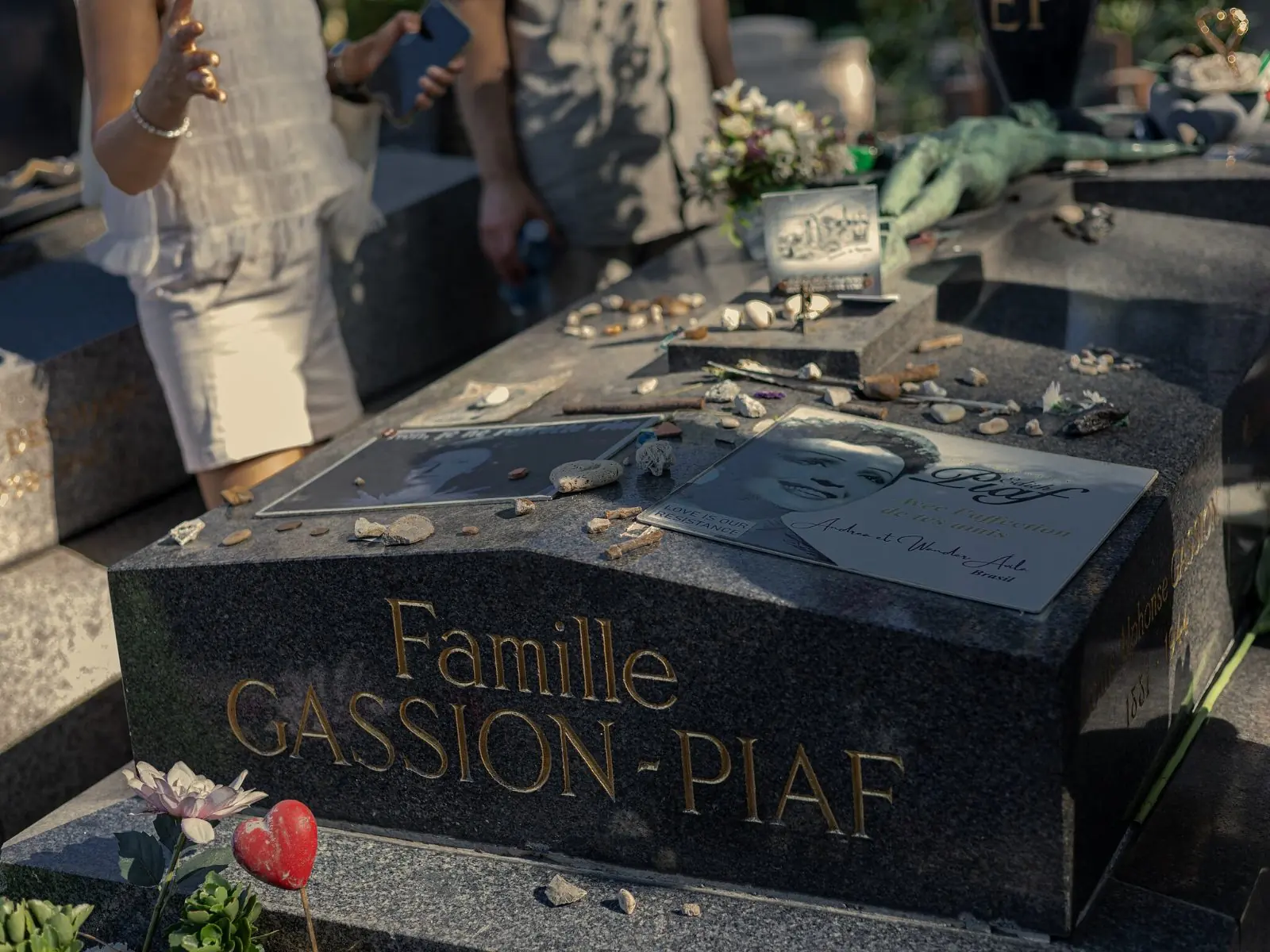 The gilt lettering of the Gassion-Piaf family grave, its stone covered with pebbles and mementoes