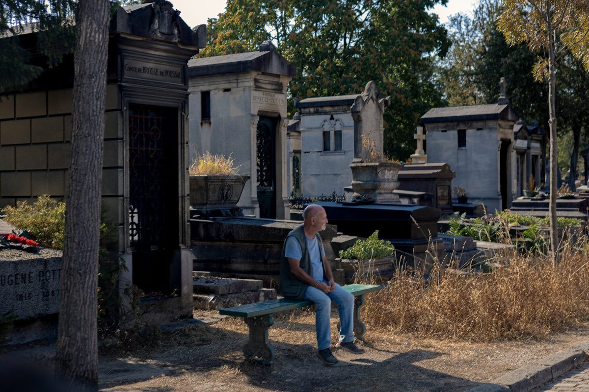 A visitor sitting alone on a stone bench among family vaults