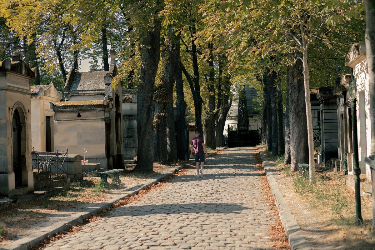 A cobbled avenue running between tombs under plane trees, a single figure in the distance