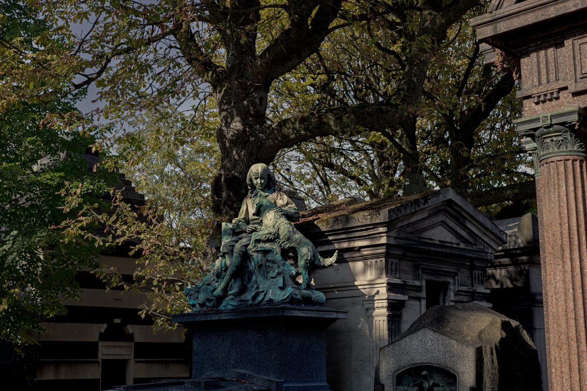 A weathered bronze sculpture of mourning figures on a family tomb, under trees