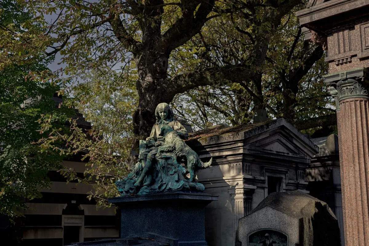 A weathered bronze sculpture of mourning figures on a family tomb, under trees