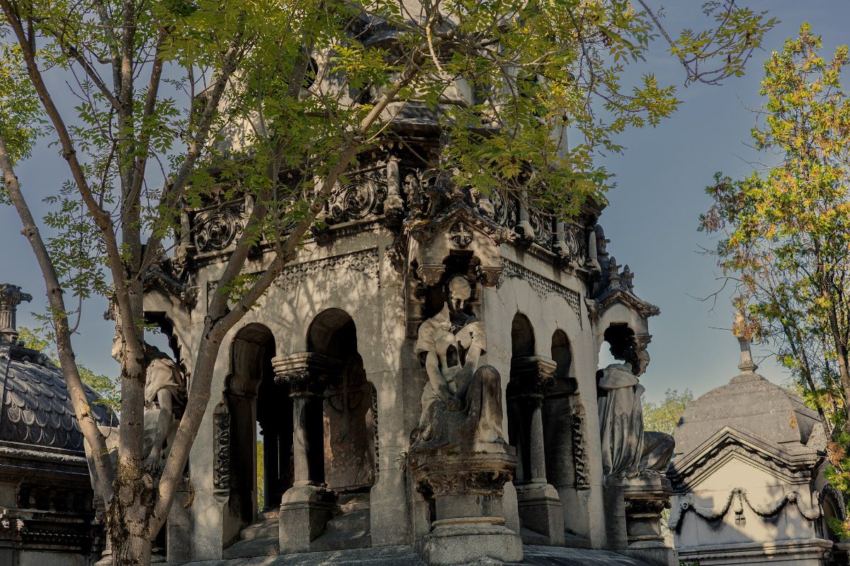 An elaborately carved stone chapel-tomb with columns and pinnacles, trees behind it