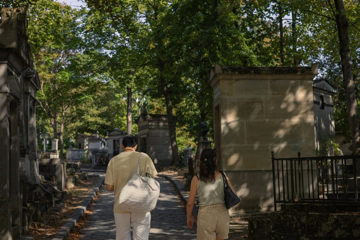 Two visitors walking up a cobbled path between family vaults and iron railings