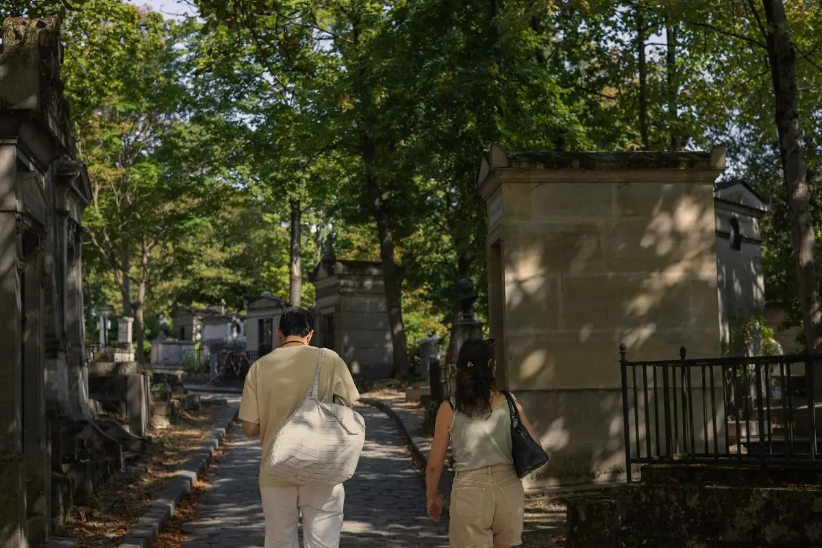 Two visitors walking up a cobbled path between family vaults and iron railings