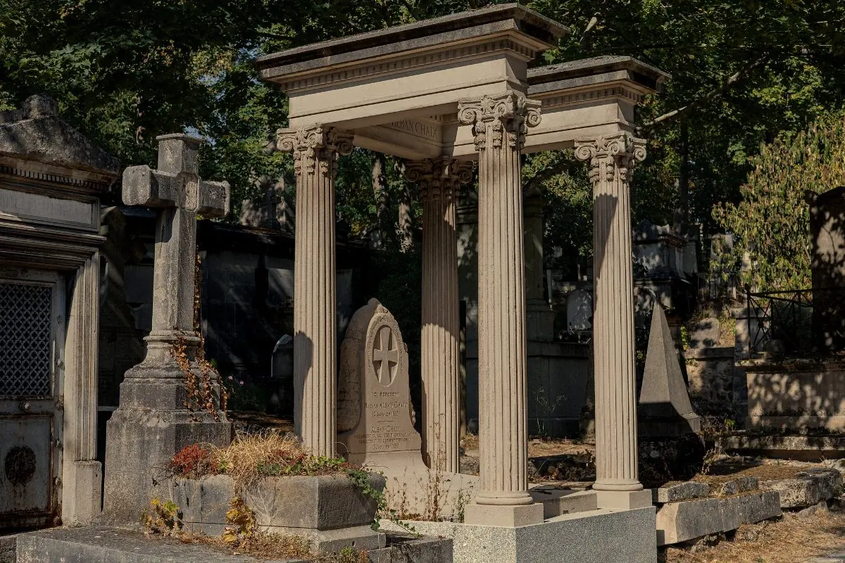 A neoclassical tomb canopy raised on columns, headstones and a stone cross around it