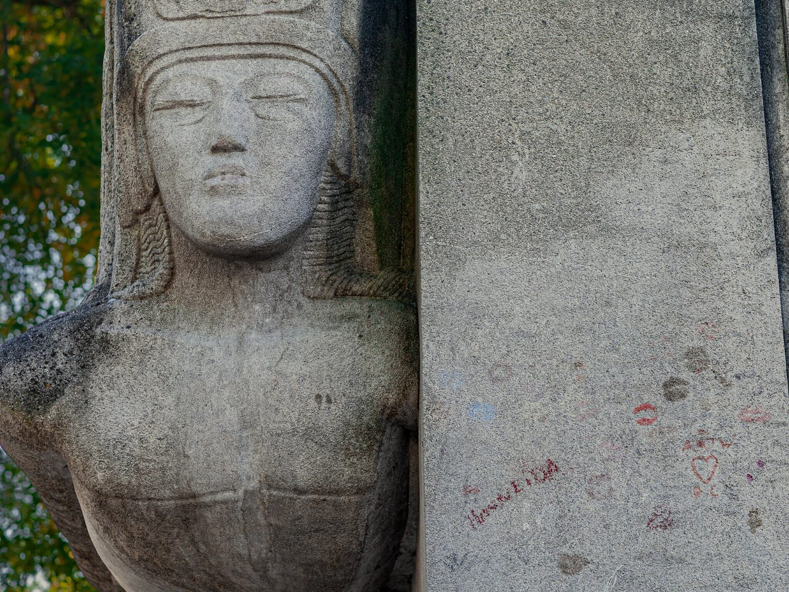 A close view of the carved face on the Wilde monument, lipstick marks on the stone above the glass barrier