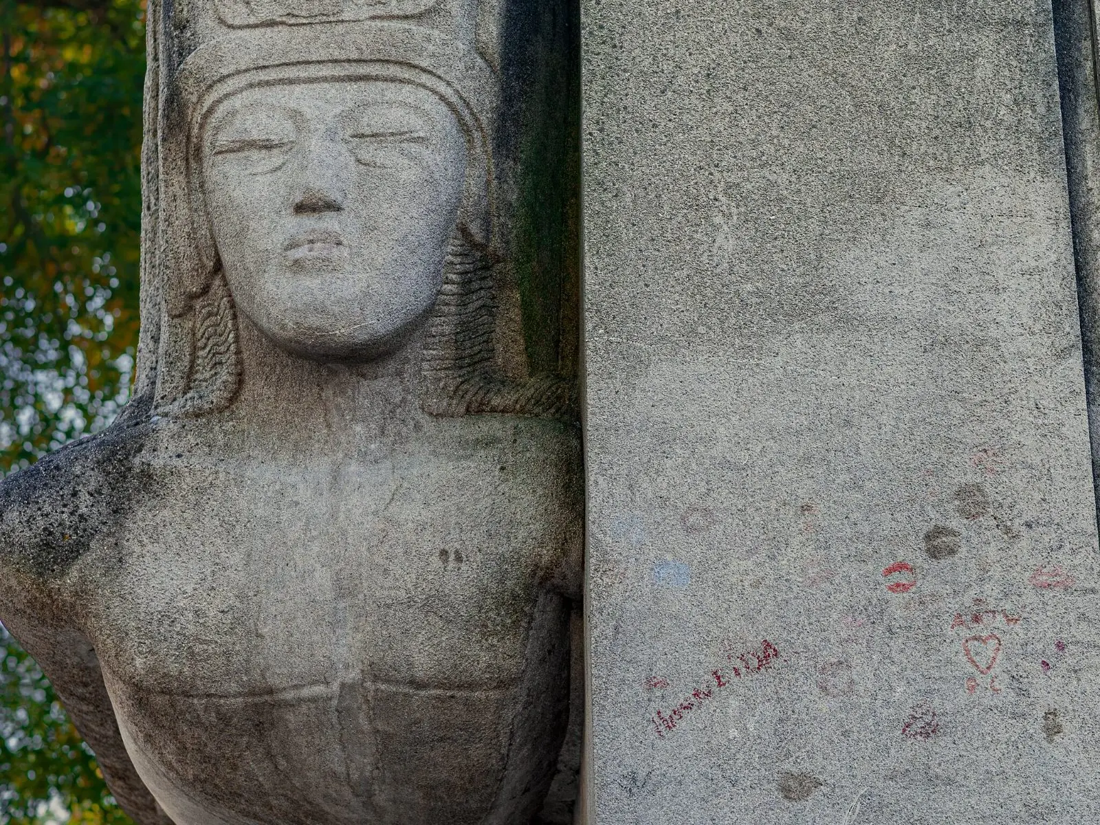 A close view of the carved face on the Wilde monument, lipstick marks on the stone above the glass barrier